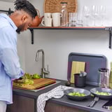 L’homme prépare de la laitue sur le comptoir de la cuisine avec un mélangeur et un saladier.