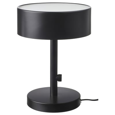 Une lampe de table NYMÅNE, noire, avec un abat-jour et une base cylindriques, en métal et en verre, fournissant une lumière douce et diffuse.
