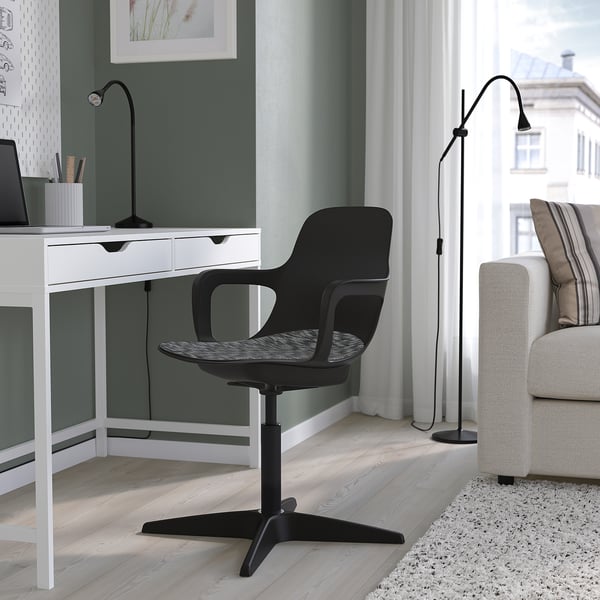 Configuration du bureau à domicile avec bureau vert, chaise noire et lampadaire. Canapé blanc avec oreillers rayés, grande fenêtre et tapis confortable.
