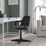 Configuration du bureau à domicile avec bureau vert, chaise noire et lampadaire. Canapé blanc avec oreillers rayés, grande fenêtre et tapis confortable.