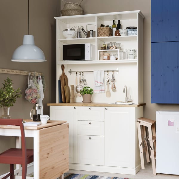 Kitchenette blanche ÖNNERUP : étagères ouvertes, armoires fermées, évier. Conception artisanale traditionnelle pour les petits espaces.