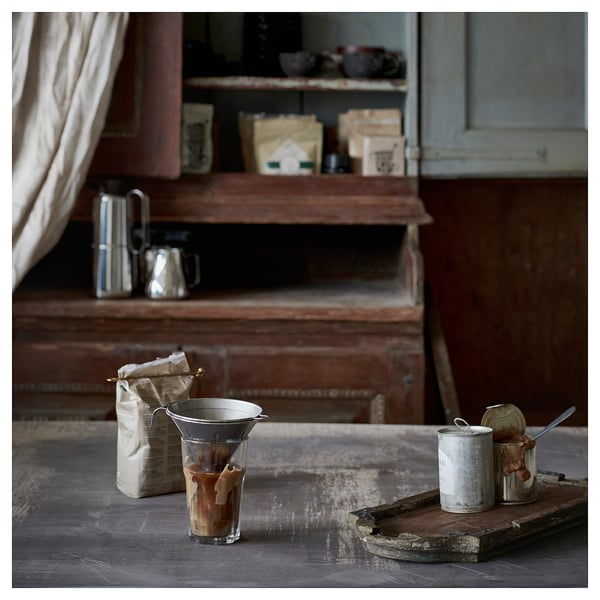 Cuisine vintage avec installation de café, y compris un filtre à café argenté, des grains en sac et des récipients avec des ustensiles sur une table en bois rustique.