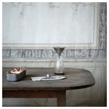 Filtre à café ÖVERST en argent sur table rustique avec serveur en verre et marc de café.
