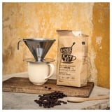 Verser sur la cafetière avec des grains de café sur une tasse contre le mur jaune.