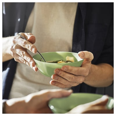 Une personne tient un bol de soupe en verre vert, à l’aide d’une cuillère. Le bol est moderne et accueillant, parfait pour un repas confortable.