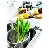 Imaginez un évier en acier inoxydable avec des oignons verts dans une passoire, des citrons et des articles de cuisine sur le comptoir.