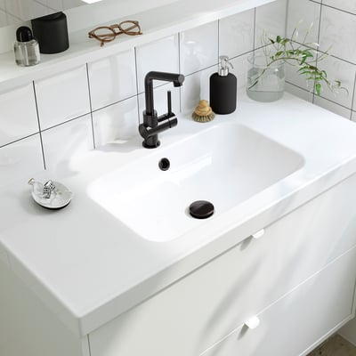 Lavabo de salle de bain blanc moderne avec robinet élégant, distributeur de savon et plante.