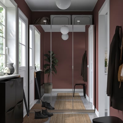 Couloir moderne avec murs marron, armoire PAX en verre, porte-manteau noir, plante en pot, bottes et vases.