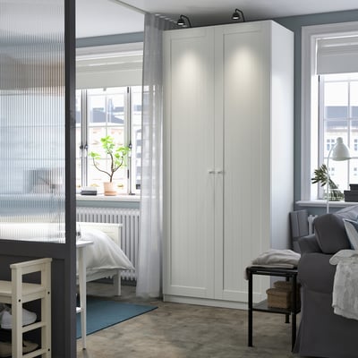 Espace de travail moderne et minimaliste doté d’une armoire PAX blanche haute et élégante, de rideaux gris et de sièges confortables. Design épuré et simple.