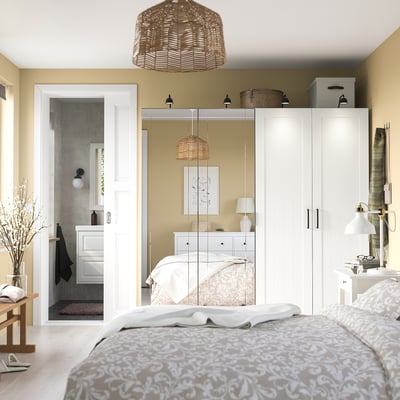 Chambre sereine avec grande armoire PAX blanche, portes en miroir, courtepointe pastel et rangement moderne.