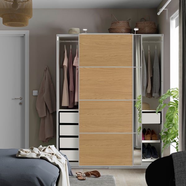 Chambre moderne avec armoire PAX en bois clair, portes coulissantes, section miroir, vêtements et tiroirs, à côté du lit.