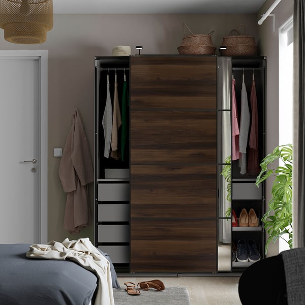 Chambre moderne avec armoire en bois sombre et en métal, portes coulissantes, vêtements suspendus et étagères à côté du lit avec literie grise / blanche.