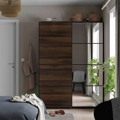 Armoire PAX en bois avec miroirs, paniers et crochets. Grand à côté du lit, reflète la pièce avec la plante et la chaise.