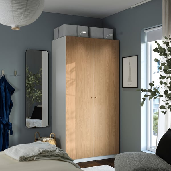 Chambre moderne avec armoire PAX, mur bleu et plante par fenêtre.