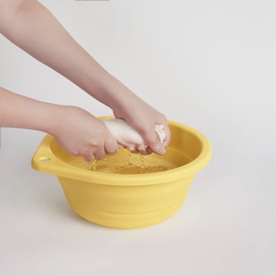 Un enfant se lave les mains dans une baignoire pliable jaune vif avec une base texturée pour frotter.