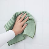 Personne tenant un chiffon en microfibre vert, côté doux pour un nettoyage en douceur, côté grossier pour les taches tenaces.