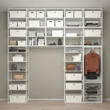 Étagères blanches bien organisées avec divers compartiments, y compris des boîtes, des livres, des vêtements et des accessoires, maximisant efficacement l’espace de stockage.