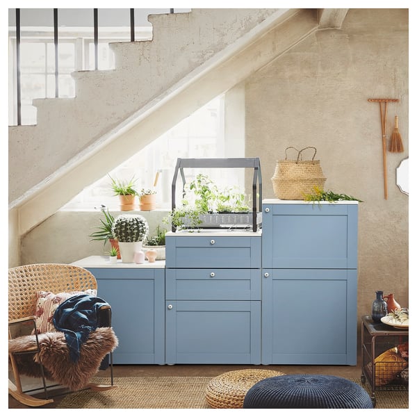 Chambre moderne avec unité de rangement PLATSA bleue sous l’escalier, avec des plantes en pot et une chaise en osier.