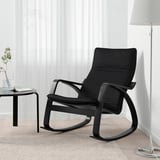 Chaise berçante noire sur un tapis, à côté d’une petite table avec un vase et une lampe.