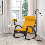 Chaise berçante POÄNG jaune vif avec cadre noir près d’une grande fenêtre. Accompagné d’une table d’appoint blanche avec des fleurs. Moderne, confortable et accueillant.