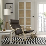 Salon moderne avec chaise POÄNG en cuir noir, tapis rayé, parquet et lumière naturelle.