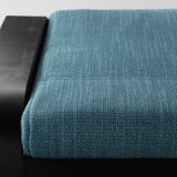Un siège rembourré bleu sarcelle avec dossier en bois noir, montrant un tissu de haute qualité et un cadre robuste.