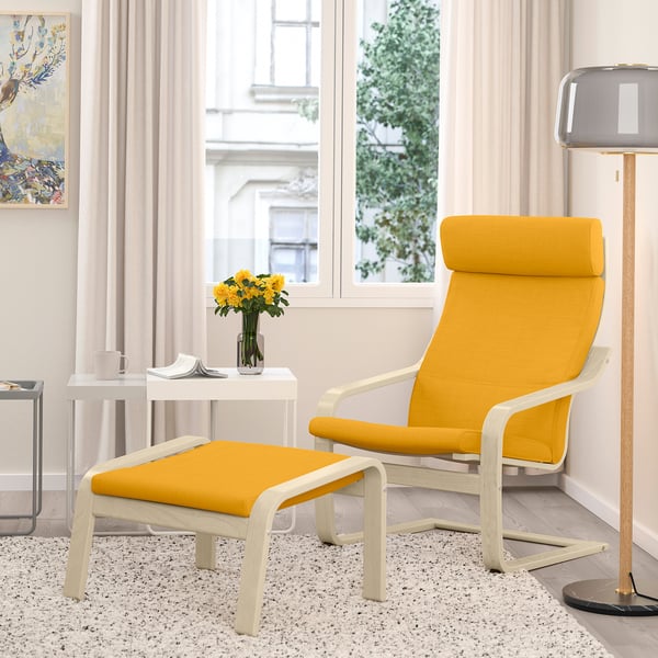 Fauteuil POÄNG jaune moutarde avec pouf, coussins épais, cadre en bois clair, fenêtre à rideaux blancs.