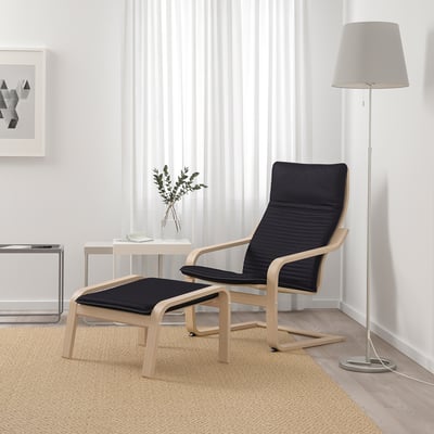 Salon moderne : chaise POÄNG noire et pouf avec cadre en bois clair, rembourré, près de la lampe et de la plante.