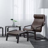 Salon moderne avec chaise POÄNG en cuir marron, repose-pieds, table d’appoint, plante, livre, lampe et tapis.