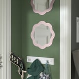Miroirs à fleurs roses sur le mur vert, en dessous se trouvent un sac vert, un fourre-tout rayé et un tableau effaçable à sec noir / blanc à côté de la porte.