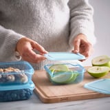 La personne place un couvercle sur un récipient alimentaire bleu avec des tranches de pomme, mettant en valeur le stockage pratique des aliments.