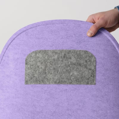 Main posant un coussin d’assise gris sur une chaise violette, montrant sa fonction antidérapante.