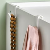Un cintre blanc au-dessus de la porte tenant une écharpe rose. Il démontre l’aspect fonctionnel de l’organisation et du rangement faciles des accessoires.