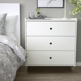Coffre RACKNÄS blanc minimaliste à côté du lit. Trois tiroirs, design élégant, petit et pratique.
