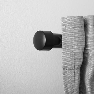 Fleuron noir sur rideau gris, mur blanc. Collection RAPHIG, look moderne.