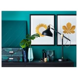 Lampe de bureau noire élégante, RANARP, contre un mur turquoise avec des impressions d’art. Design réglable, moderne et élégant, parfait pour la lecture.