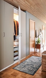 Armoire moderne avec porte REINSVOLL gris-beige, design minimaliste, vêtements ouverts révélateurs, posé sur parquet, tapis bleu.