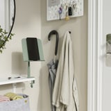 Entrée avec support de tablette bleu clair pour une utilisation mains libres, étagère blanche, patère avec manteau beige, clés et une plante.