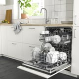 Lave-vaisselle ouvert dans la cuisine propre, rempli d’assiettes et de tasses blanches, plus petites que l’évier, sous le comptoir.