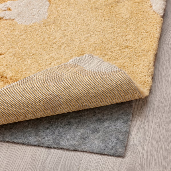 Tapis jaune et blanc avec différentes hauteurs de poils sur plancher de bois franc, sous-couche antidérapante grise visible.