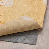 Tapis jaune et blanc avec différentes hauteurs de poils sur plancher de bois franc, sous-couche antidérapante grise visible.