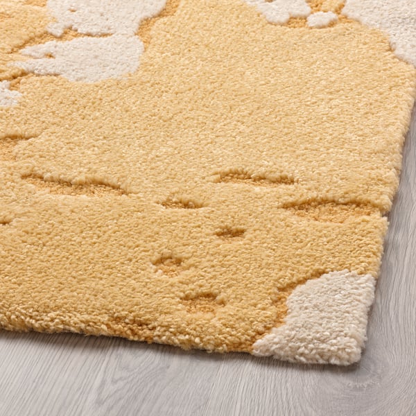 Tapis doux et texturé jaune et blanc avec des hauteurs de poils variées, reposant sur un plancher en bois.