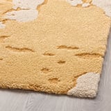 Tapis doux et texturé jaune et blanc avec des hauteurs de poils variées, reposant sur un plancher en bois.