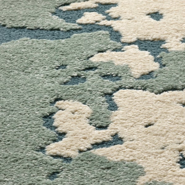 Tapis abstrait avec mélange de poils hauts/bas. Matériaux doux et respectueux de l’environnement. Nuages blanc cassé sur fond vert.