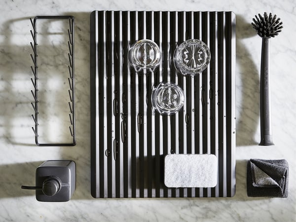 Accessoires de cuisine noirs, y compris séchoir, brosse, porte-éponge et épurateur sur une surface en marbre.