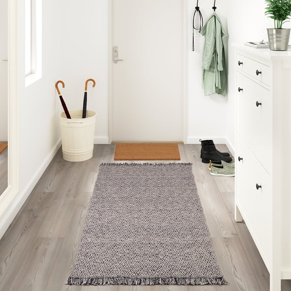 Entrée avec tapis RÖRKÄR, rangement blanc, bottes, plante et manteaux.
