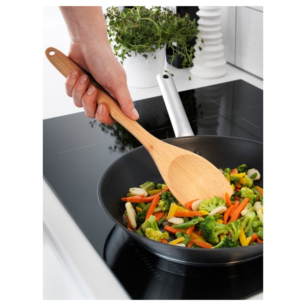 À l’aide d’une cuillère RÖRT en bois, une main remue les légumes dans une poêle noire sur une cuisinière. La cuillère est douce pour les surfaces antiadhésives.