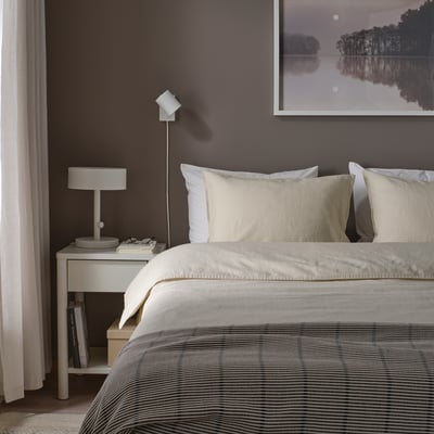 Chambre avec couette RUNDHAGTORN sur grand lit, literie rayée, oreillers clairs, mur gris, photo minimaliste, table de chevet avec lampe et livres.