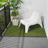 Petite chaise en plastique blanc sur tapis de gazon artificiel vert près de la balustrade noire.