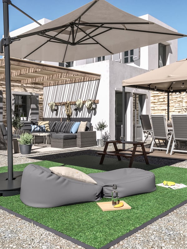 Cour arrière avec bordure grise RUNNEN, gazon artificiel, table de pique-et meubles de patio sous parasol beige.